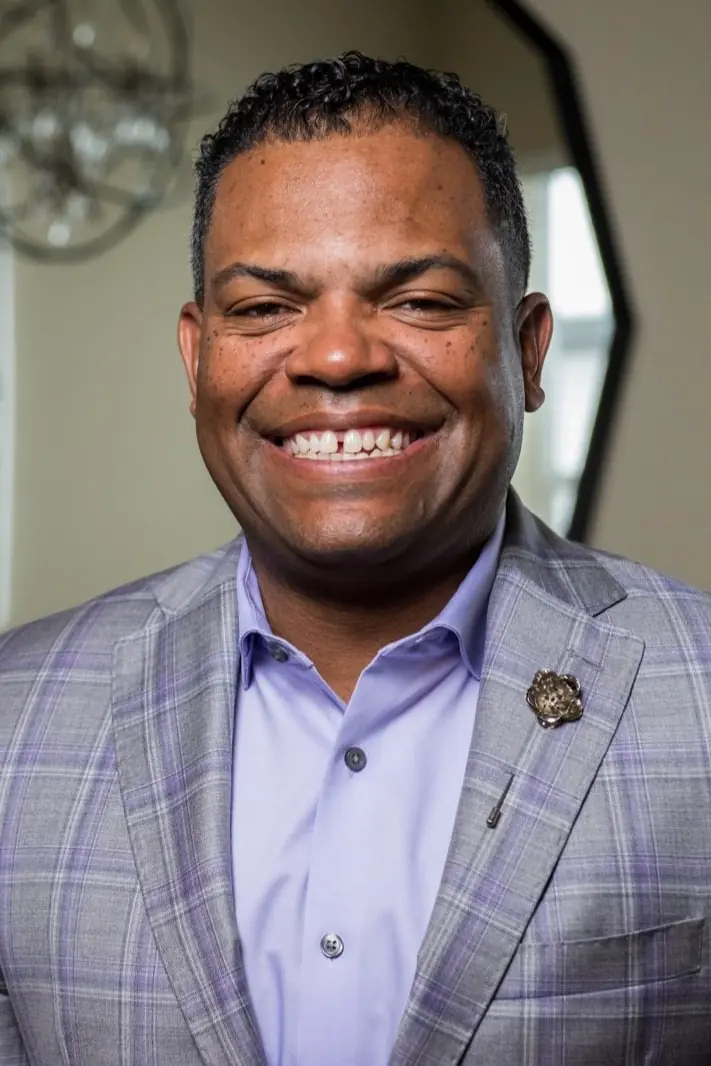 Jason O. Harris, keynote speaker, smiling in a grey and purple plaid jacket and a lavender shirt